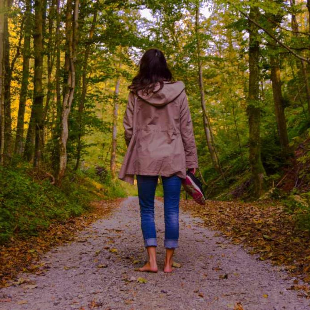 Woman standing on a pathway barefoot in the woods with her shoes in her hand