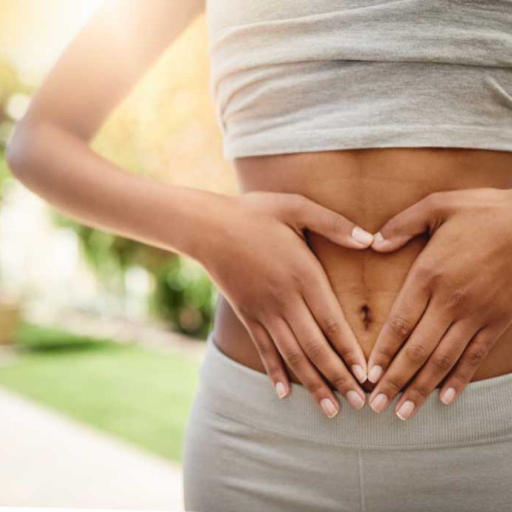 close up of woman's stomach as she's holding her hands in a heart shape