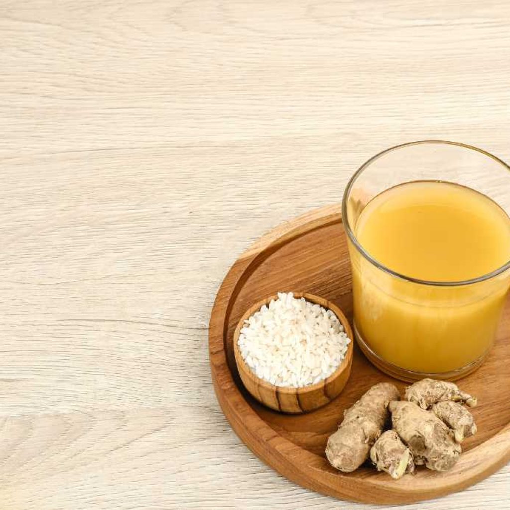 wood tray with ginger, a glass of orange substance, and pieces of raw ginger