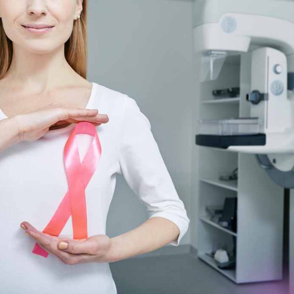 Woman holding large pink breast cancer ribbon in exam room