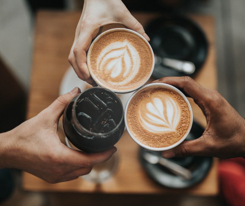 3 people clinking their coffees together