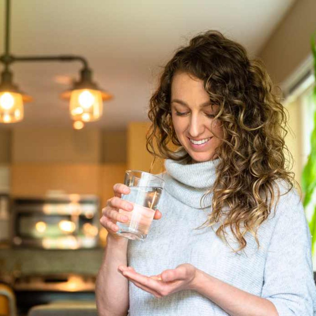 woman holding a glass of water and has her hand cupped like she is about to take medicine