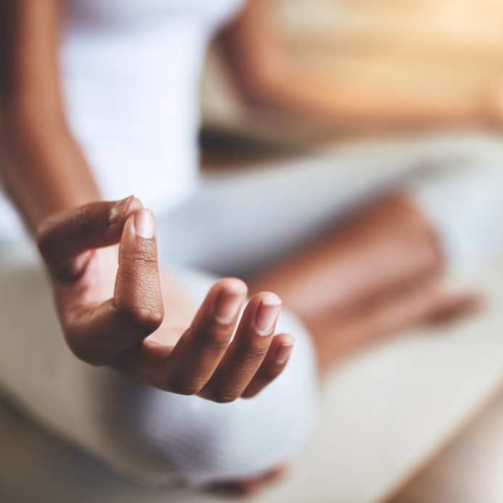 Close-up of a person's hand resting on their knee in a meditation pose, with the fingers gently touching in a mudra