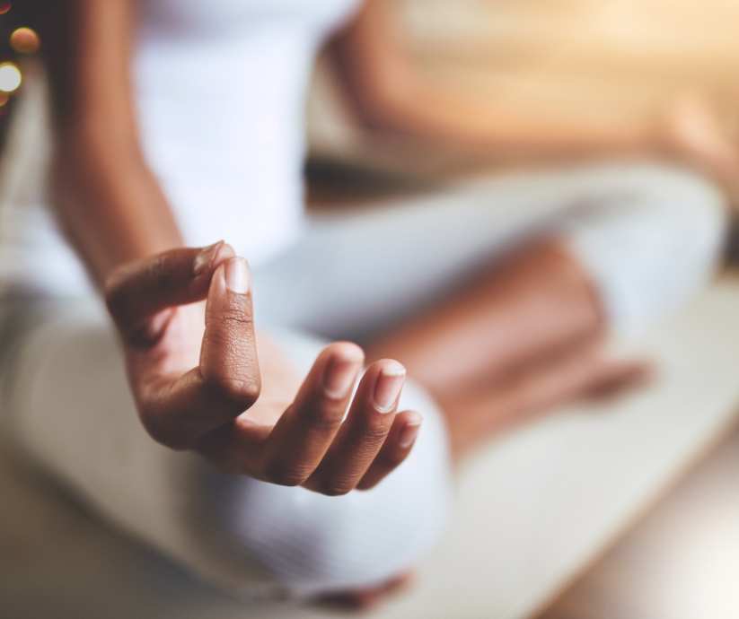 Close-up of a person's hand resting on their knee in a meditation pose, with the fingers gently touching in a mudra