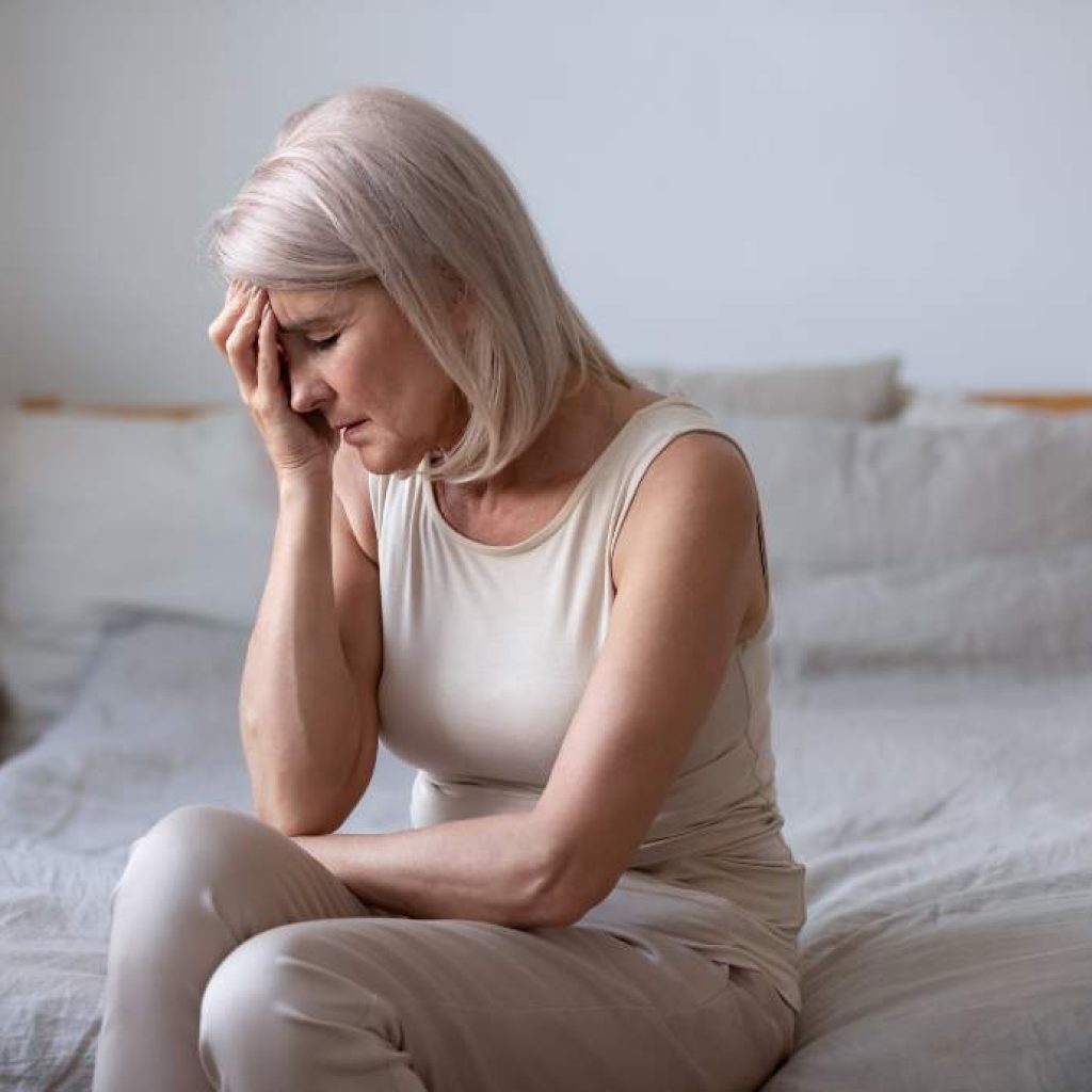 Older woman on bed holding her head in pain