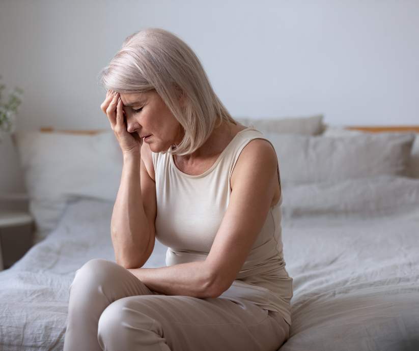 Older woman on bed holding her head in pain